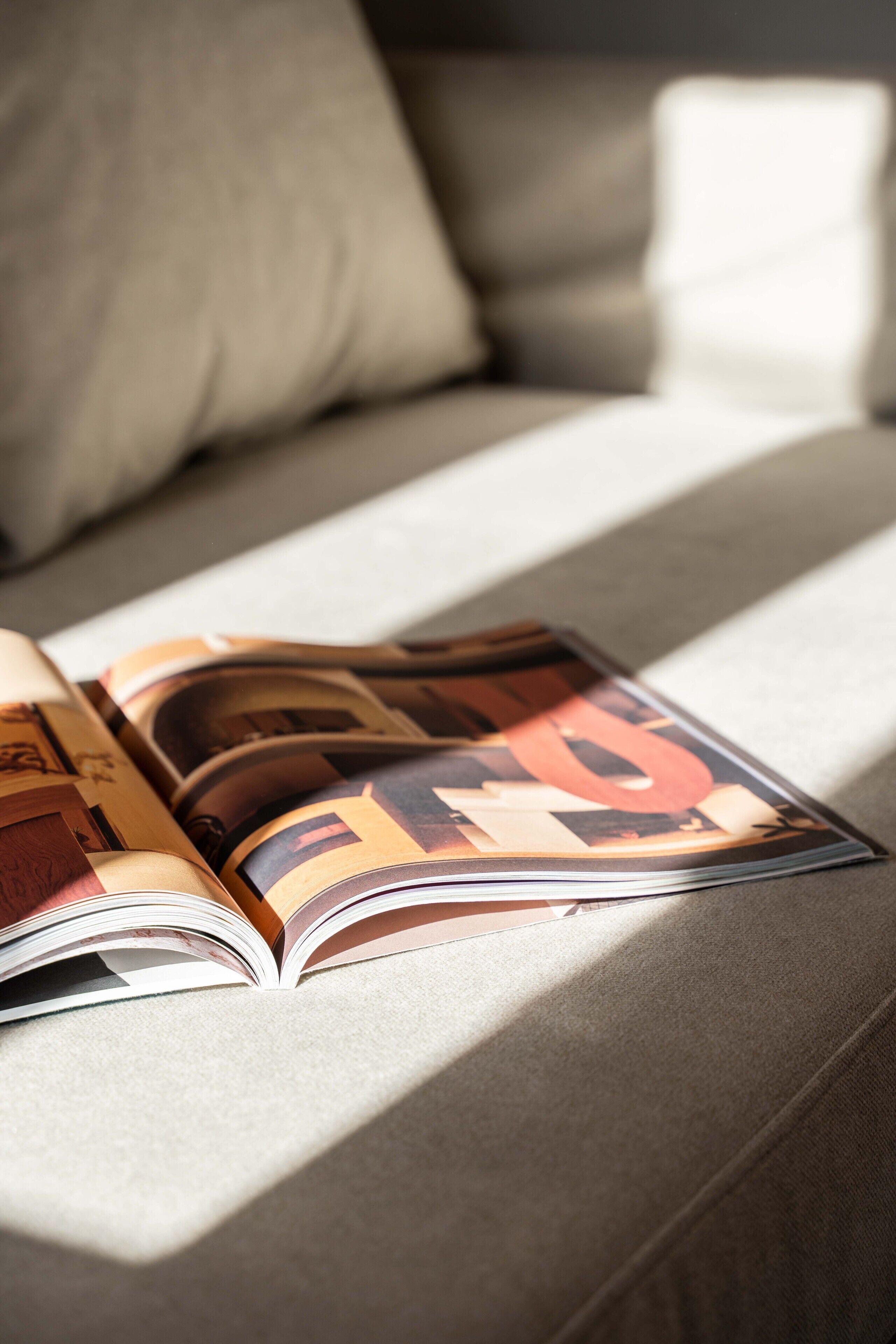 An open magazine on a sofa with a cushion.