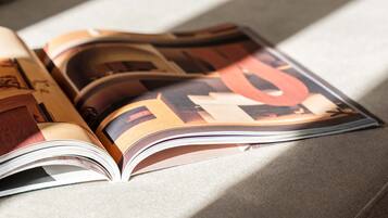 An open magazine on a sofa with a cushion.