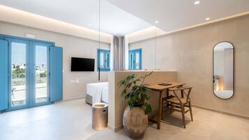 Moderni hotellihuone, jossa on sänky, työpöytä tuolilla, suuri peili ja ruukkukasvi.
