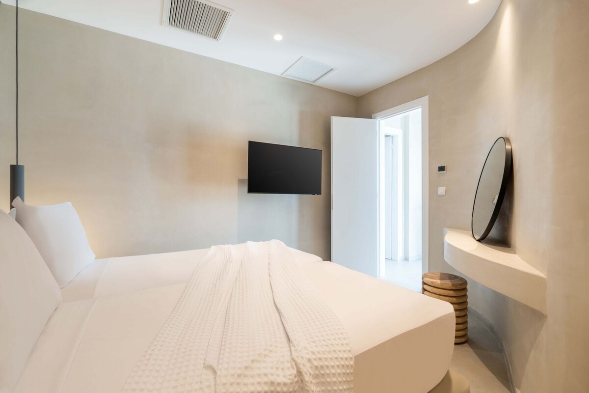 A modern bedroom with a large bed, a mounted TV, and a mirror on the wall.