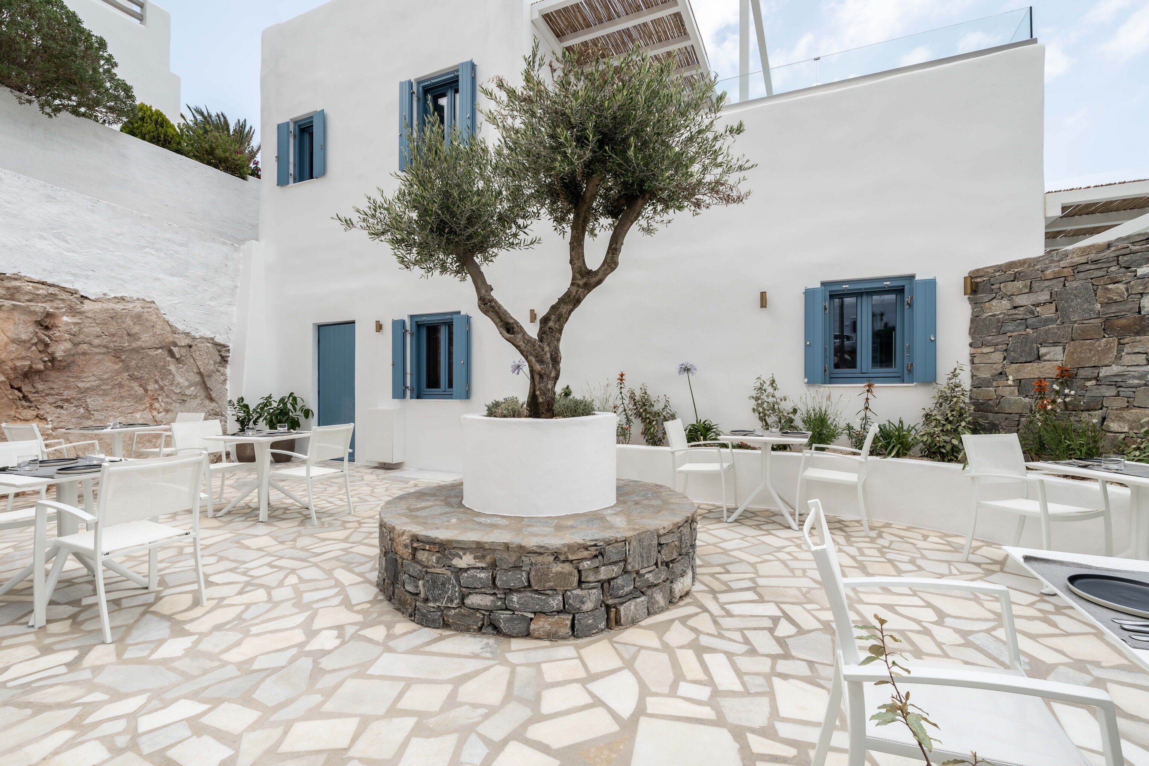 Un patio con paredes blancas, contraventanas azules, suelo de piedra y mobiliario exterior.