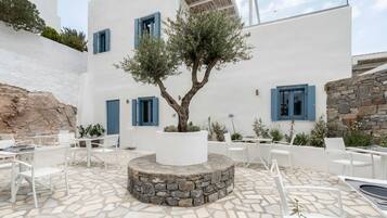 Un patio con paredes blancas, contraventanas azules, suelo de piedra y mobiliario exterior.