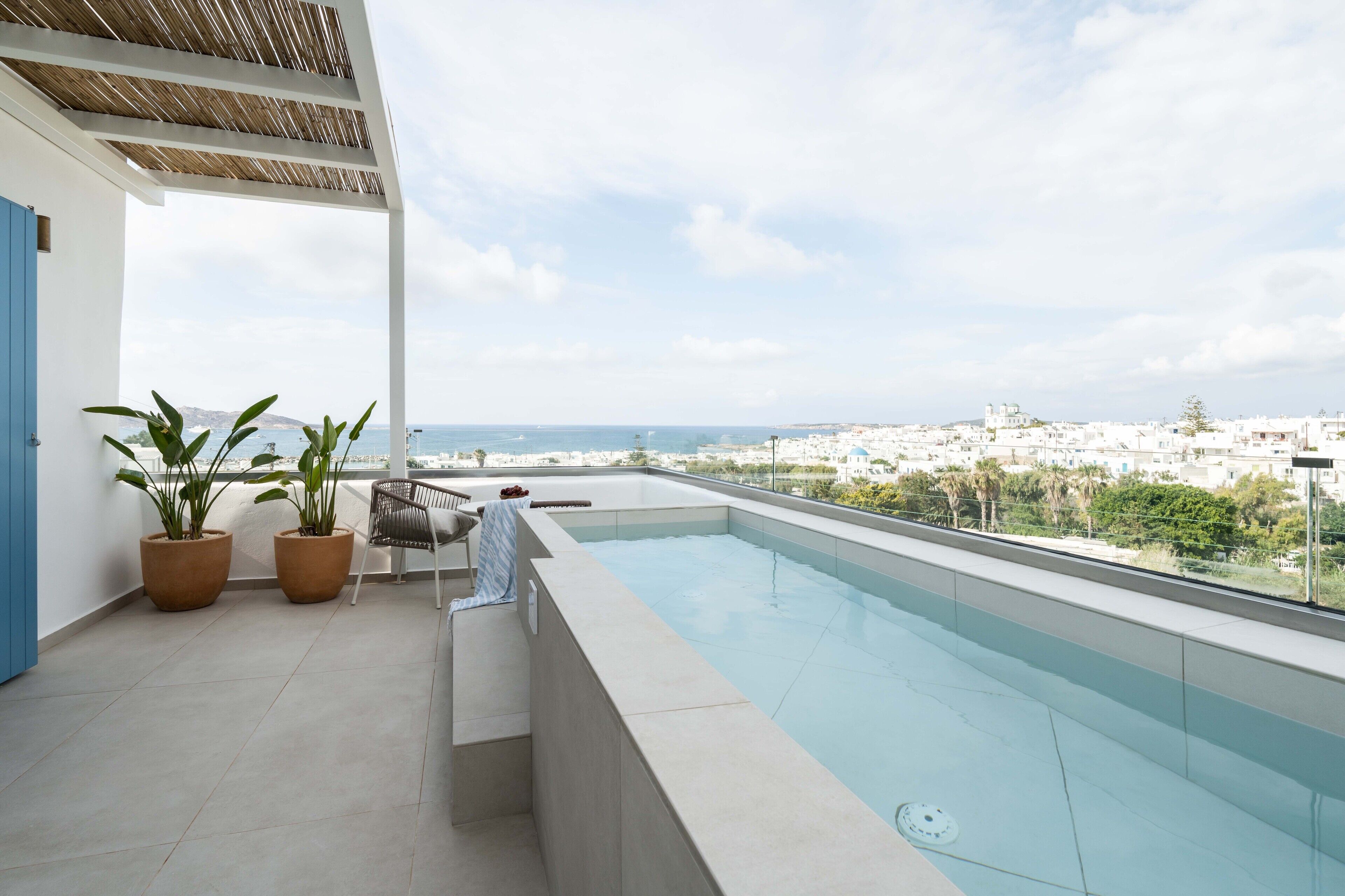 Une piscine sur le toit, agrémentée de plantes en pot, d’une chaise et offrant une vue sur la ville.