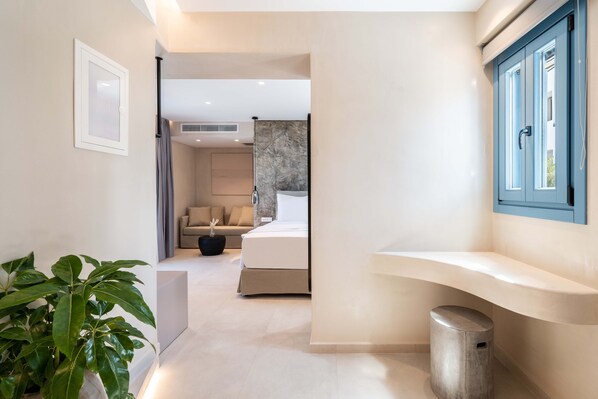 Une chambre d’hôtel moderne avec un lit, un petit coin salon, une salle de bain avec une porte bleue et une plante en pot.