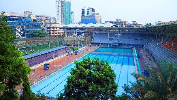 An indoor swimming pool with multiple lanes, surrounded by spectator seating and a covered area. - Turtle Hotel (Mumbai)