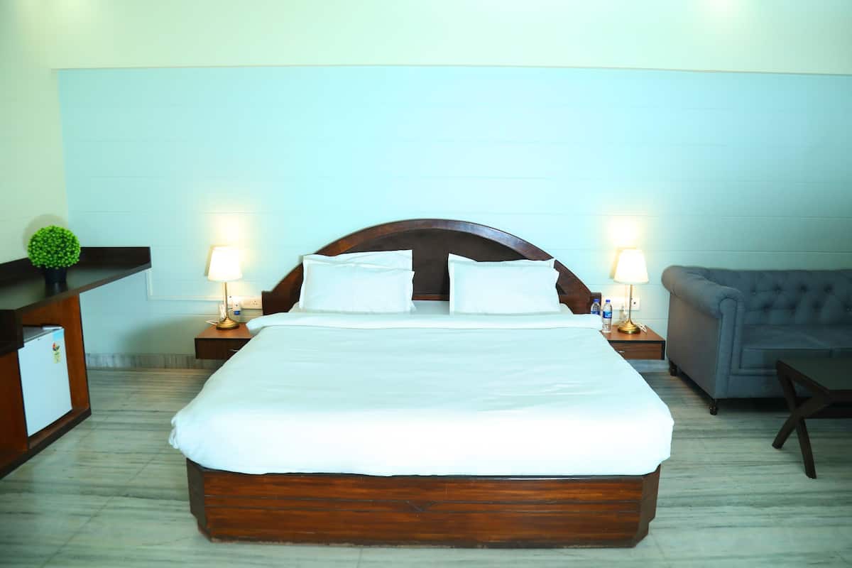 A neatly made bed with white linens, two bedside lamps, a grey sofa, and a small table.