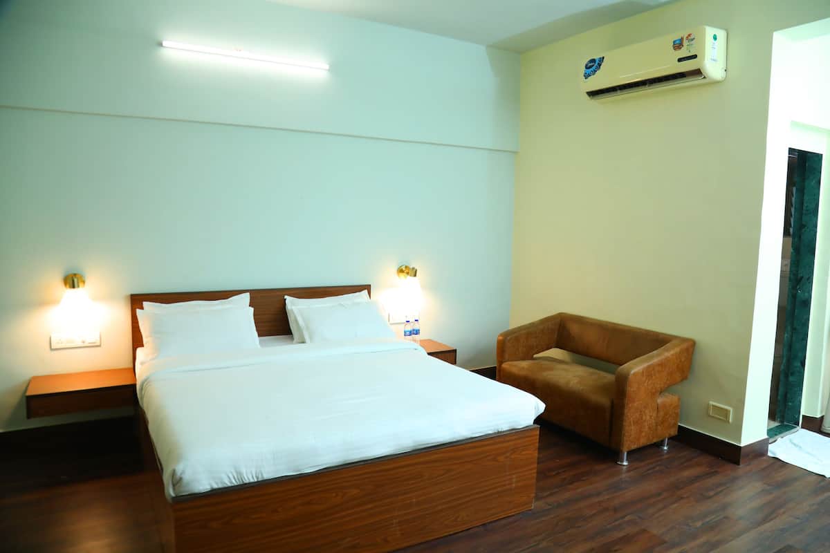 A hotel room with a wooden bed, two bedside lamps, a brown armchair, and an air conditioning unit on the wall.