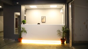 A reception area with a white counter, two potted plants, a framed picture, and a ceiling-mounted security camera. - Turtle Hotel (Mumbai)