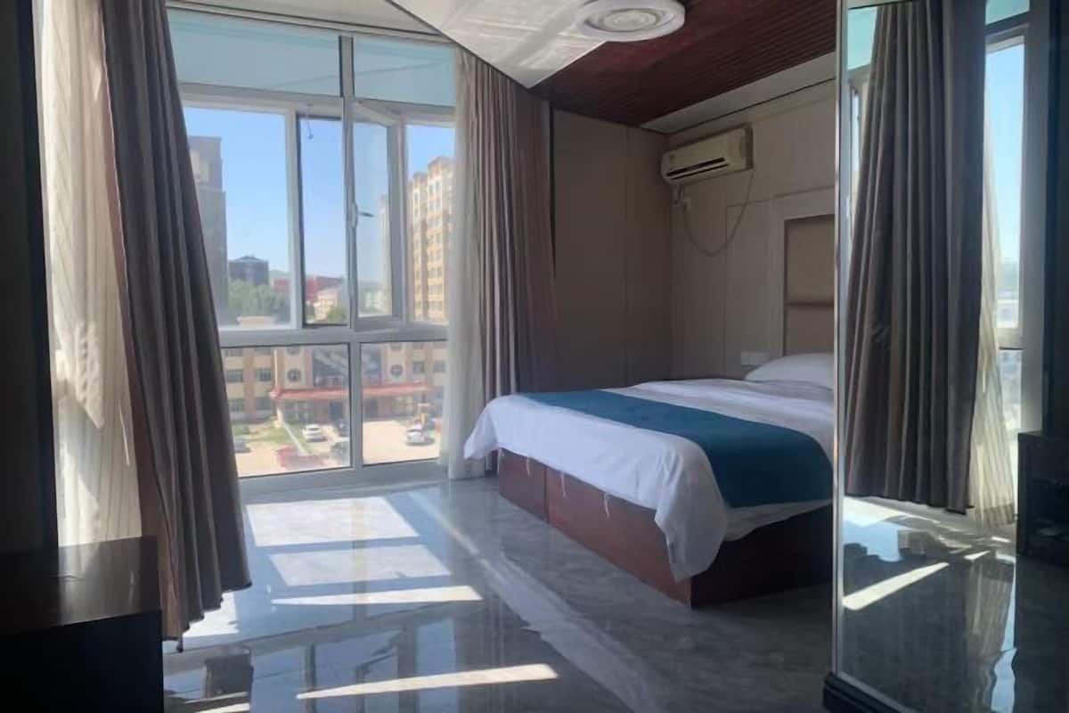 Una habitación de hotel con una cama, un ventanal grande y un equipo de aire acondicionado.