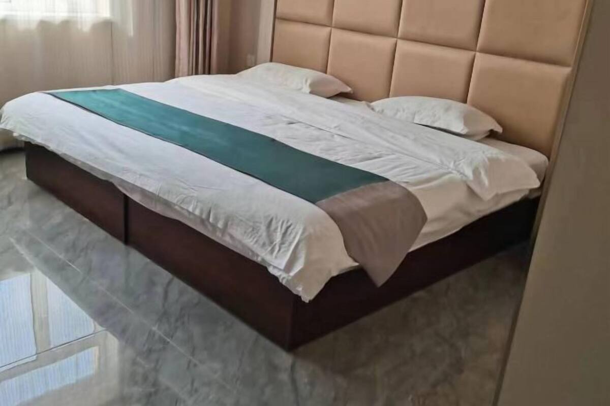 Una cama con cabecera, una colcha blanca y azul turquesa, y suelo de mármol.