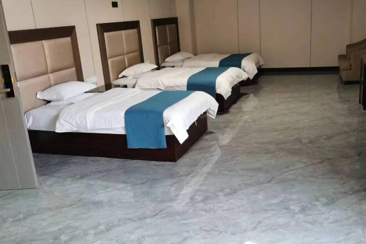 Habitación de hotel con tres camas, piso de mármol y cabecera de madera.