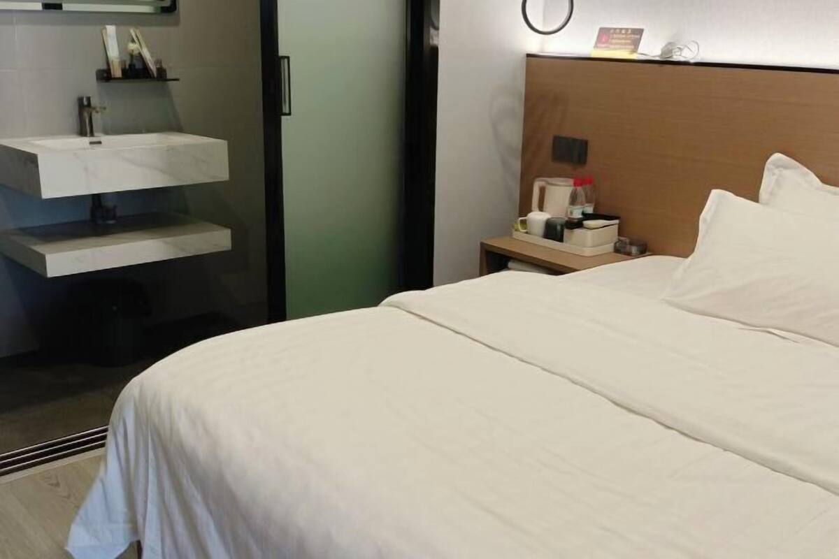 A hotel room with a bed, a nightstand, a mirror, a wall-mounted shelf, and a door.
