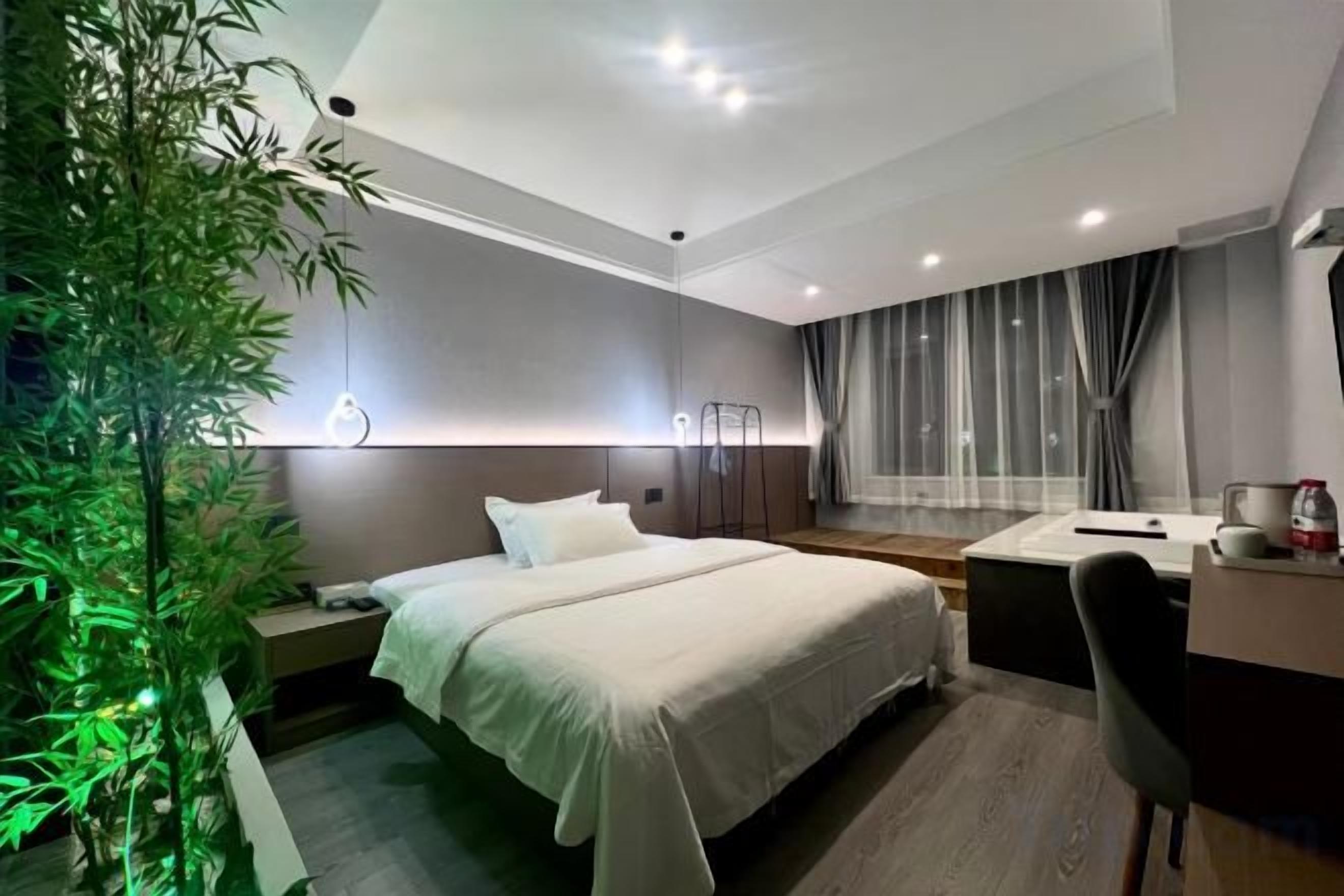 Een moderne hotelkamer met een bed, nachtkastje, bureau, stoel en een groot raam met gordijnen.