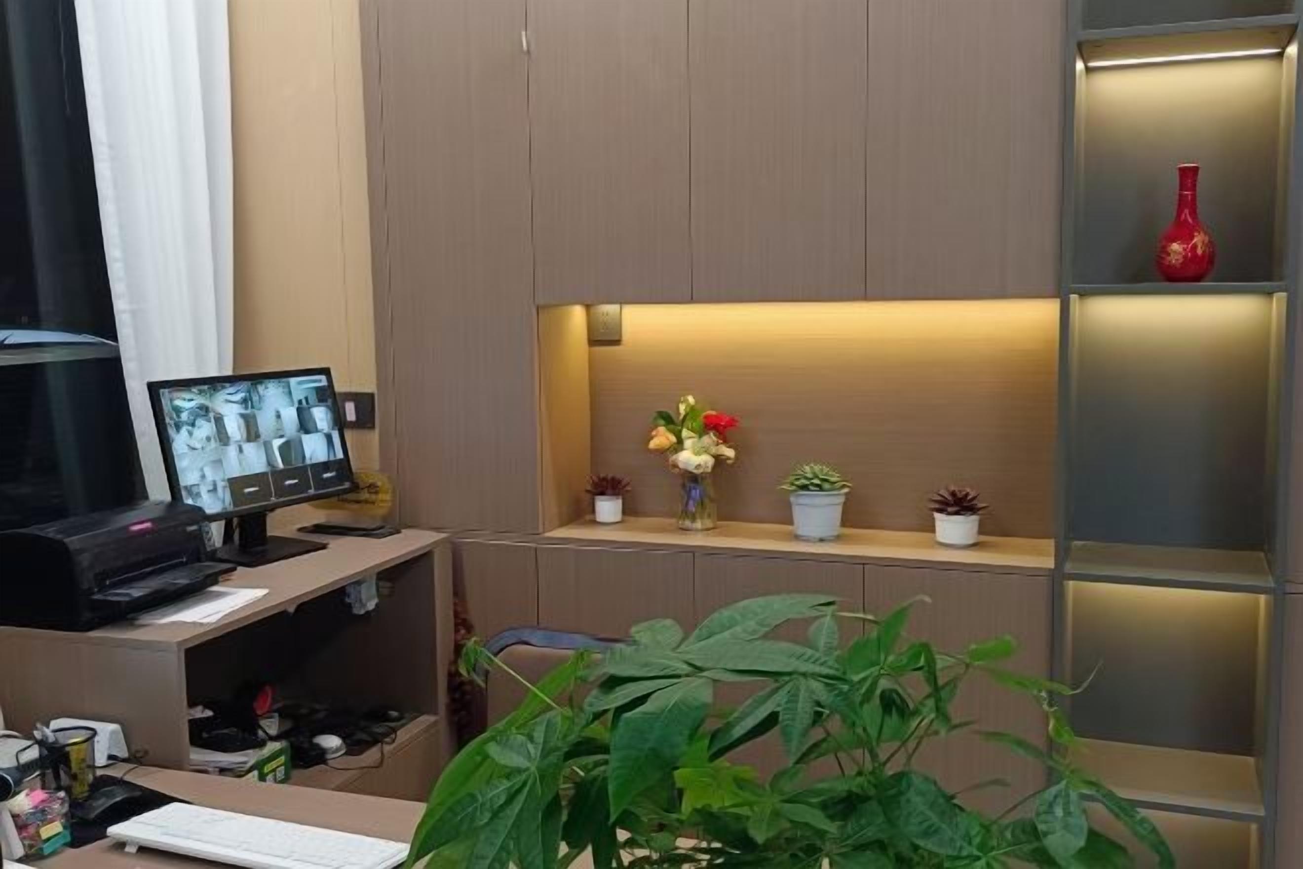 A hotel room with a desk, computer, and a shelf with decorative items.