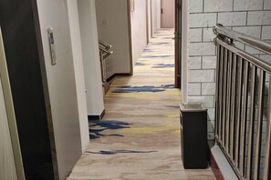 A hallway with a patterned floor, doors on the left, and a trash bin on the right. - an County Zhengxing Business Hotel (Mianyang)