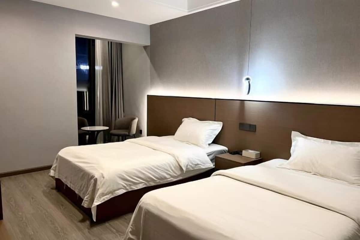 A hotel room with two beds, a small table, a chair, and a nightstand.
