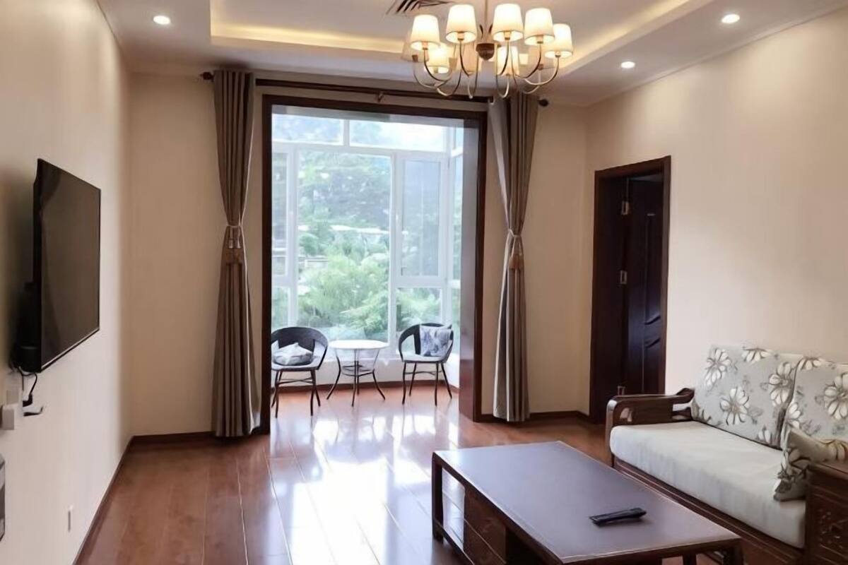 A living room with a flat-screen TV, a sofa, a coffee table, and a dining area with chairs.