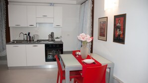 A modern kitchen with white cabinets, a stove, and a dining area with red chairs and a white table. - Romantic apartment with canal view (Venezia)