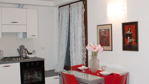 A modern kitchen with white cabinets, a gas stove, and a dining area with a table and red chairs. - Romantic apartment with canal view (Venezia)
