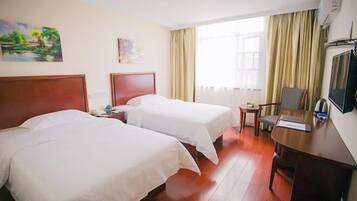 A hotel room with two beds, a desk, a chair, a TV, and a window with curtains.