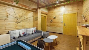 A cozy room with wooden walls, a sofa with Paris-themed cushions, a small pool table, and a door with a round clock.