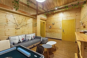 A cozy room with wooden walls, a sofa with Paris-themed cushions, a small pool table, and a door with a round clock. - Menglonglie Hotel (Rongjiang)