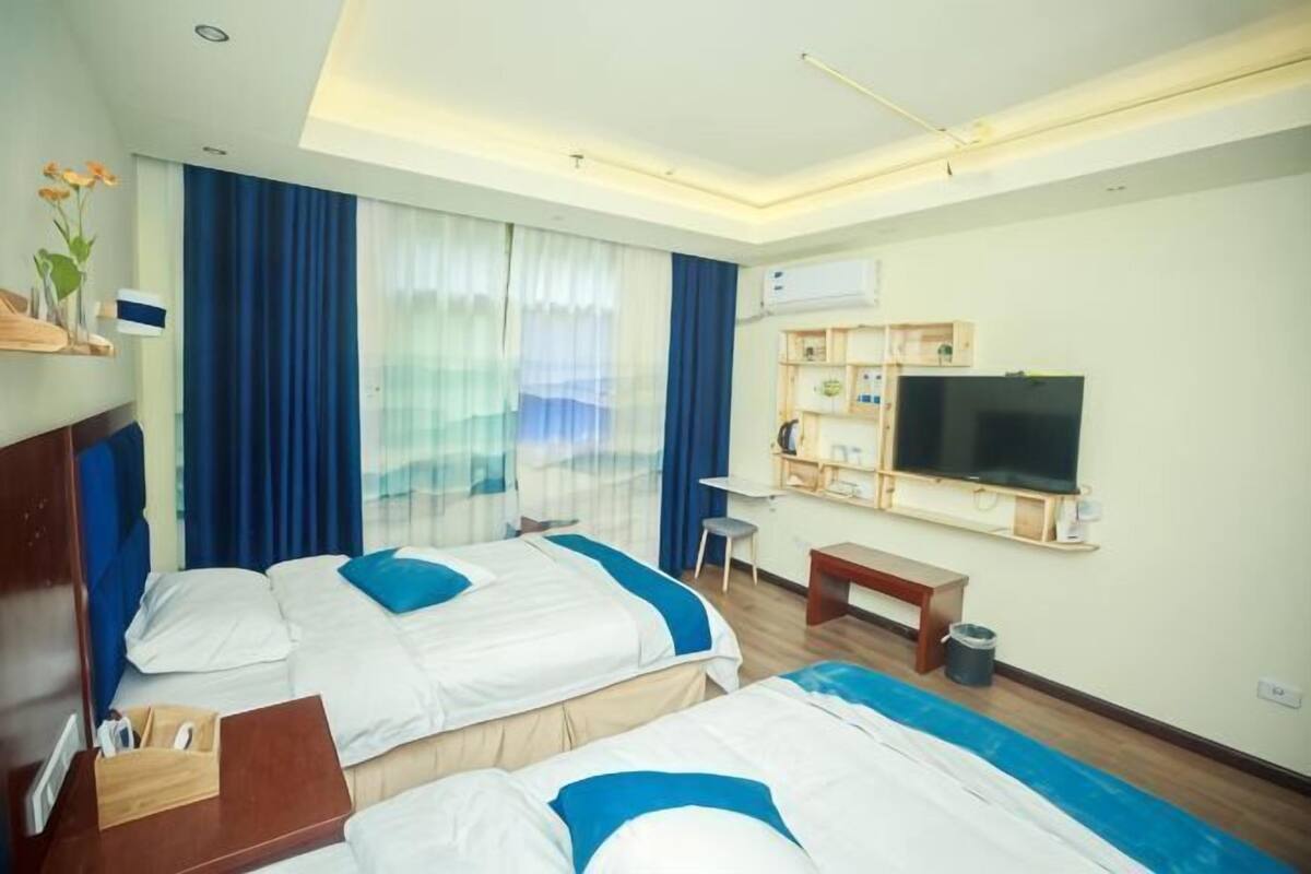 A hotel room with two beds, a desk, a TV, and a ceiling light fixture.