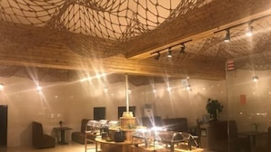 Un interior moderno con techo de madera, una mesa de madera central con objetos encima y varias zonas de estar.