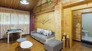Una habitación acogedora con techo de madera, un sofá gris con almohadas de la Torre Eiffel, una mesita pequeña y una ventana con cortinas ligeras.
