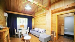 A cozy cabin interior with a wooden floor, a sofa, a dining table with chairs, and a small round table.