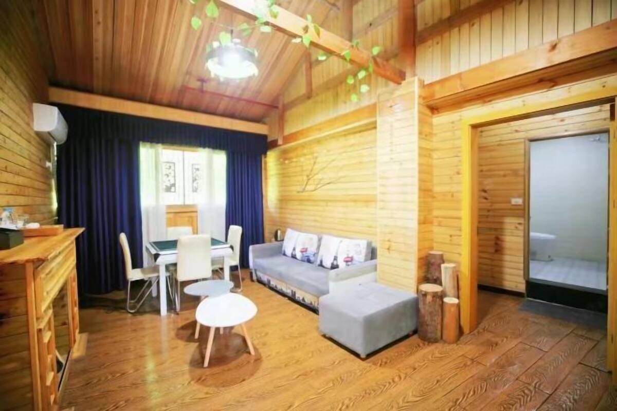 A cozy cabin interior with a wooden floor, a sofa, a dining table with chairs, and a small round table.
