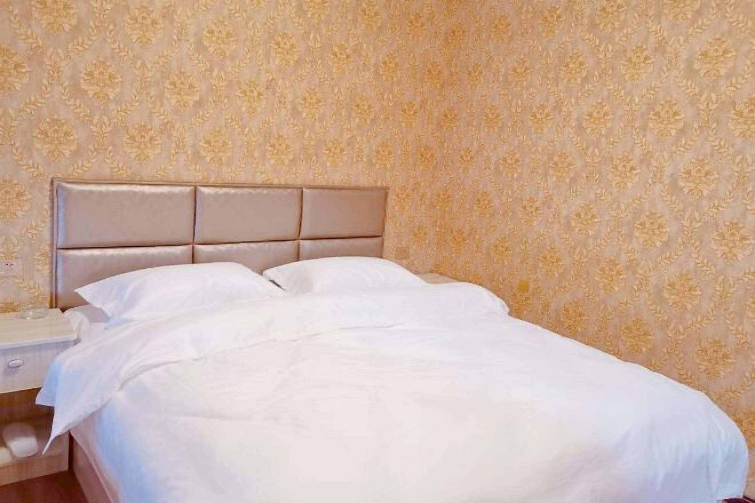 A neatly made bed with a headboard, a bedside table, and a wall with a floral pattern.