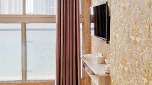A hotel room with a large window, a mounted TV, and a vanity with toiletries.