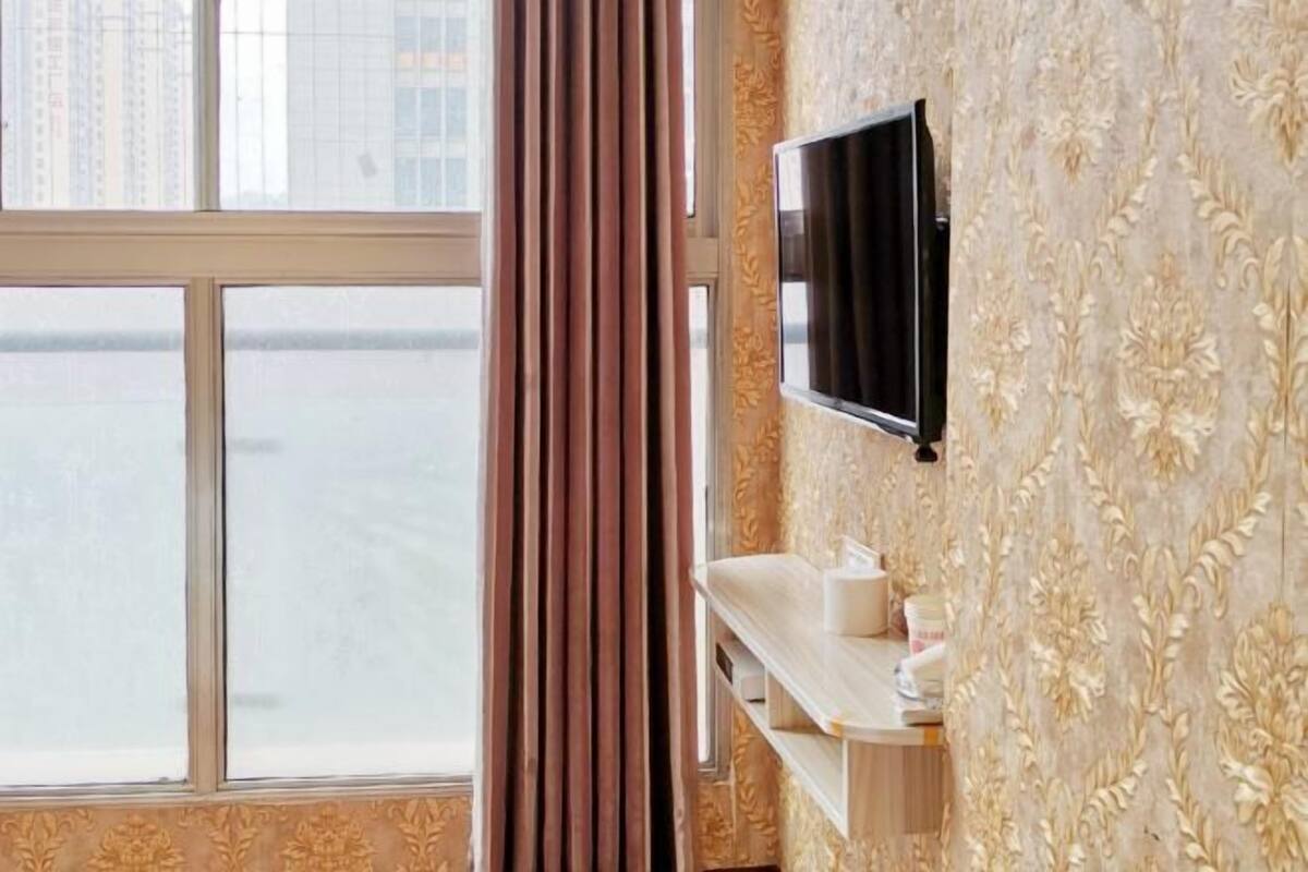 Una habitación de hotel con un ventanal grande, un televisor montado y un tocador con artículos de aseo.