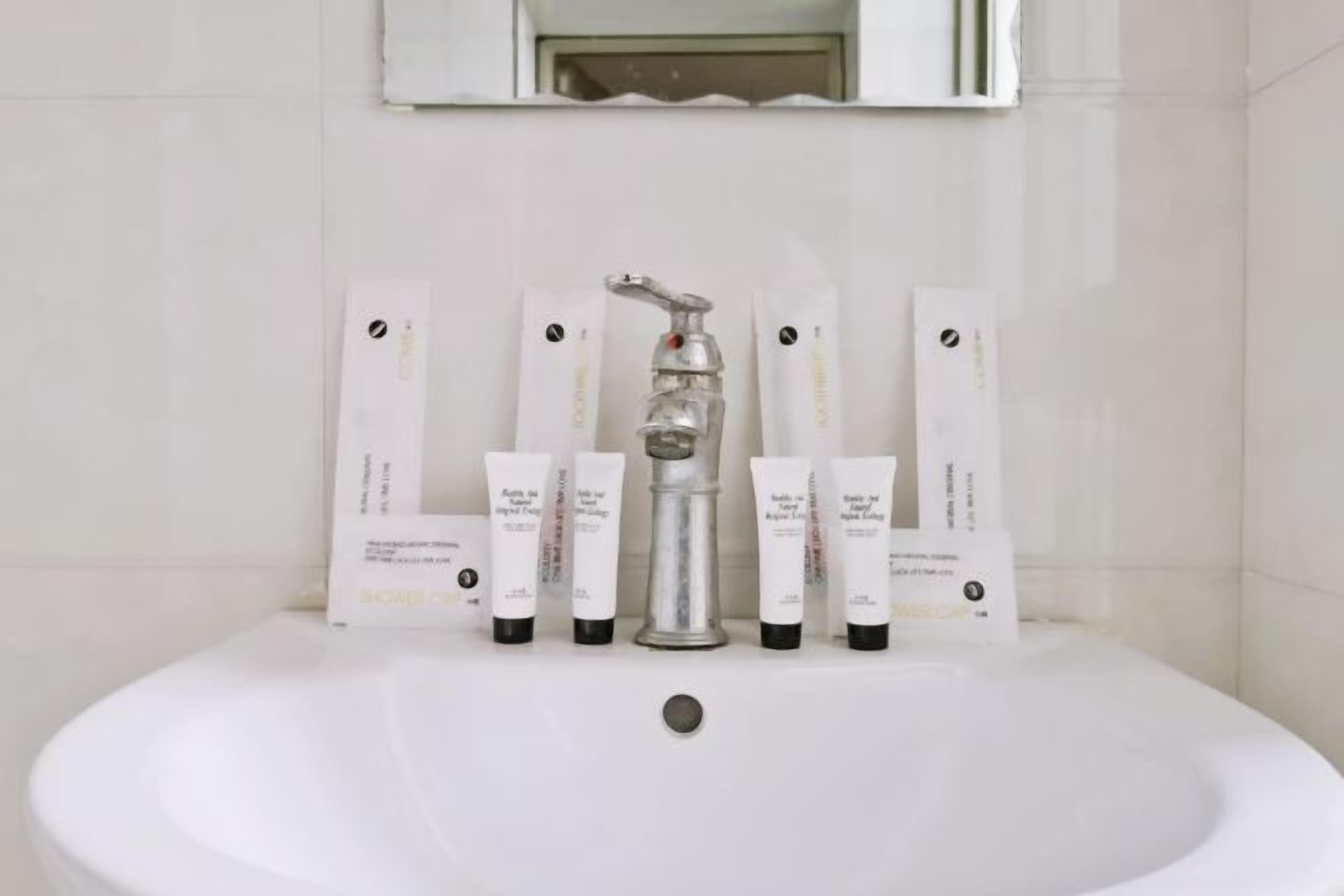 Un baño con un lavamanos blanco, un grifo de plata y seis botellas de loción blanca dispuestas en la pared.