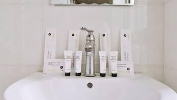 Un baño con un lavamanos blanco, un grifo de plata y seis botellas de loción blanca dispuestas en la pared.