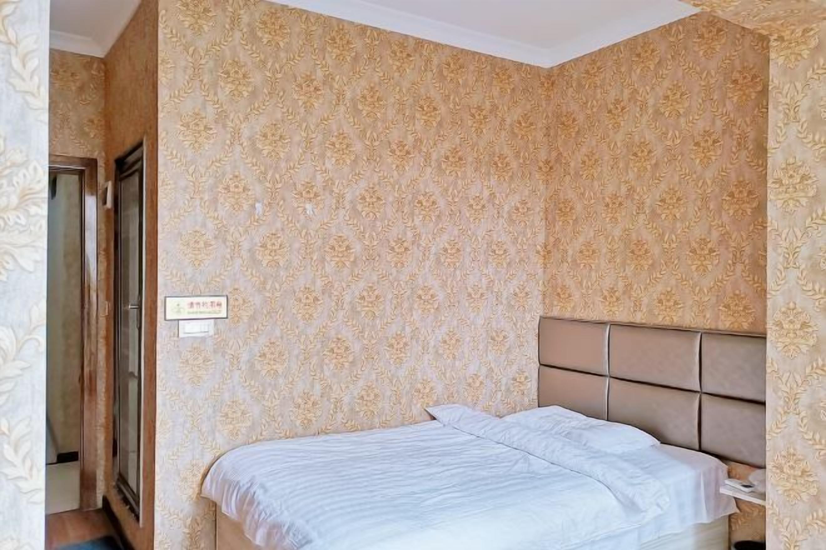 A hotel room with a patterned wallpaper, a bed with a headboard, and a door.