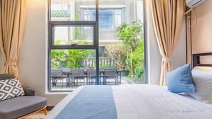 A hotel room with a bed, a sofa, a dining table, and a view of the outside. - Time Walk Guesthouse (Shenzhen)