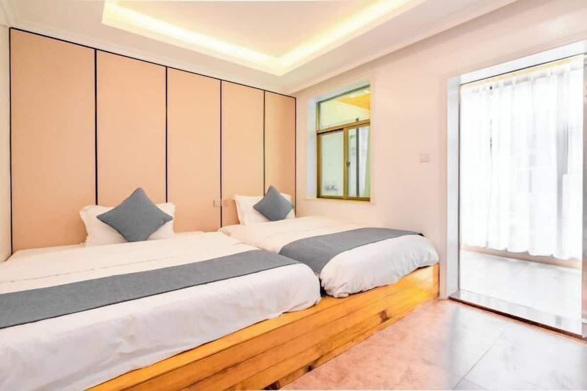 A modern hotel room with two beds, a large window with curtains, and a wooden headboard.