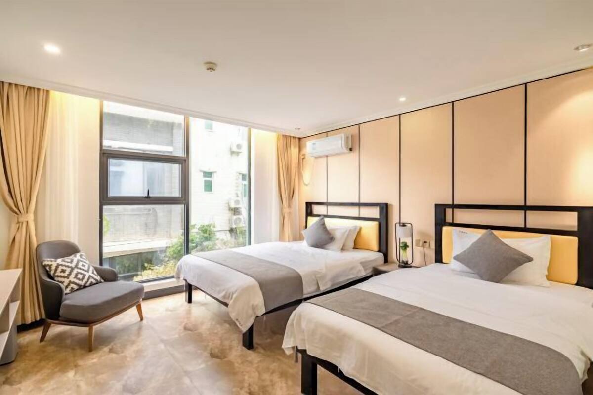 A hotel room with two beds, a chair, a window, and an air conditioning unit.