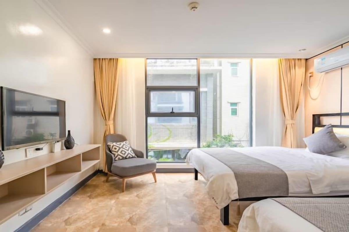 A hotel room with a bed, a TV, a chair, and a window with curtains.