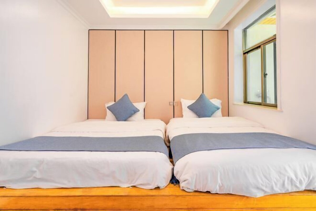 A bedroom with two beds, a wooden floor, a large window, and a ceiling light.