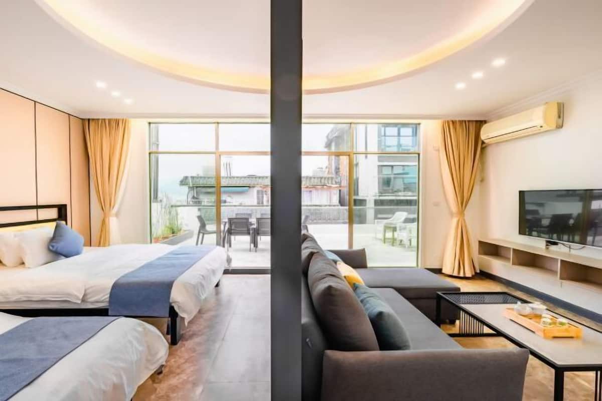 A modern hotel room with a large bed, a sofa, a TV, and a balcony with a view.