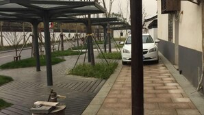 A covered outdoor area with a paved walkway, a car parked in a narrow alley, and a building with a white and grey facade. - Jinxiu Nianhua Inn (Tongxiang)