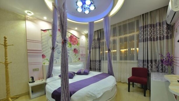 A bedroom with a round bed, a bedside table, a chair, a vanity, and a window with curtains. - Jinxiu Nianhua Inn (Tongxiang)