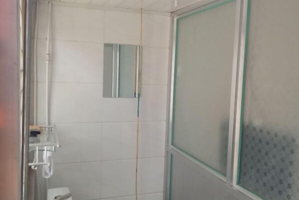 A bathroom with white tiled walls, a glass shower enclosure, and a small mirror.