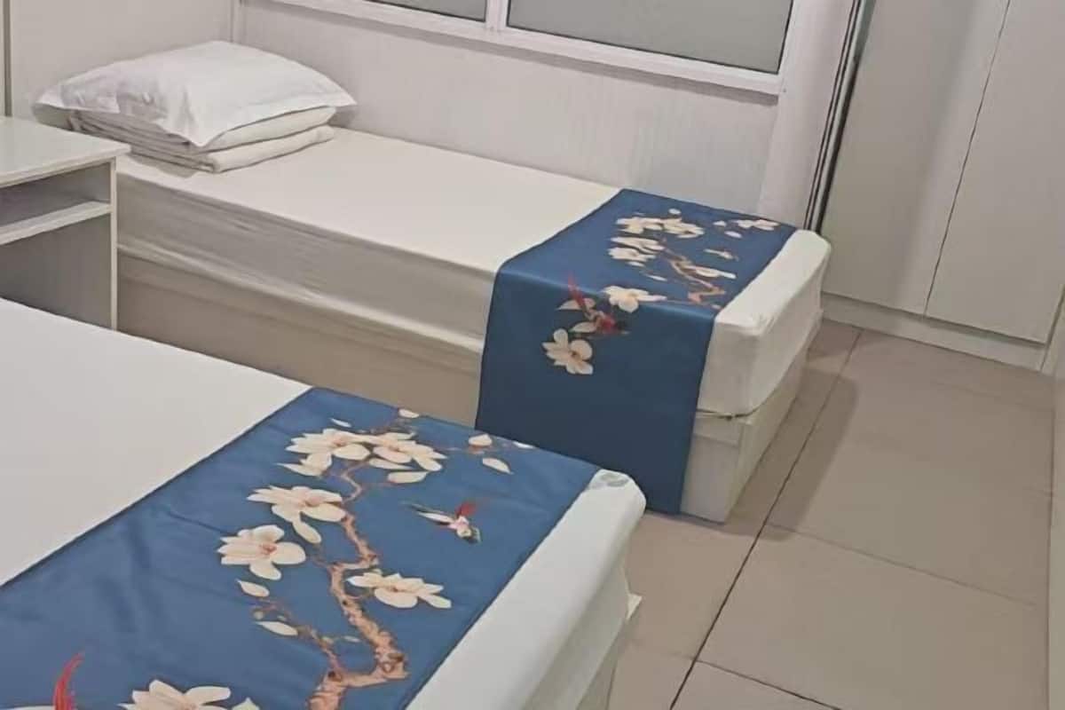 Ein Schlafzimmer mit zwei Betten, beide mit blumigem, blauem Überwurf. Auf einem Bett liegt ein weißes Kopfkissen und es gibt ein weißes Kopfteil.