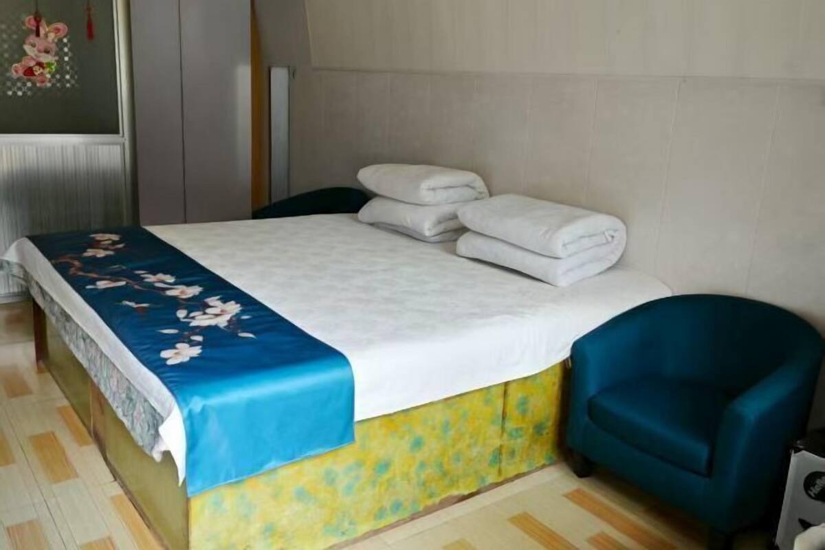 Un letto rifatto con una coperta a fiori, una sedia blu e un termosifone sullo sfondo.