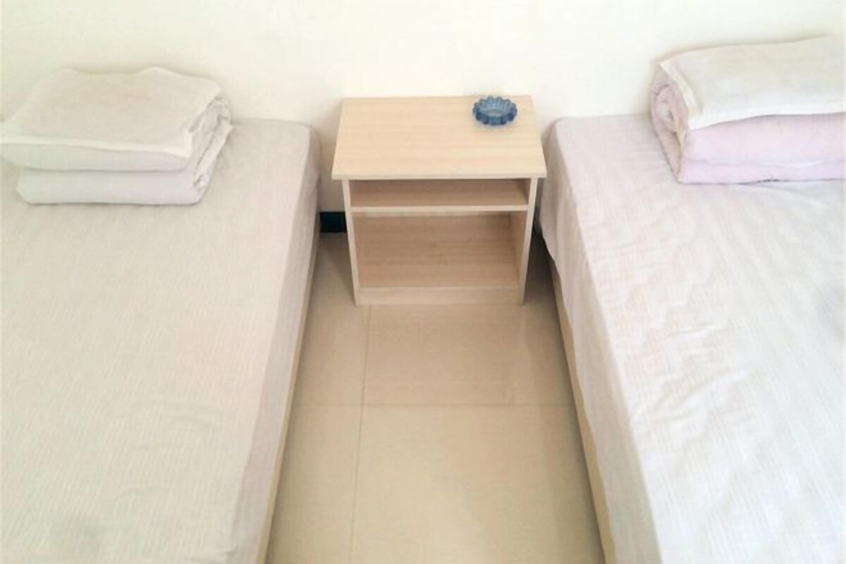 Une petite pièce unique comprenant deux lits, une table de chevet en bois et un objet bleu posé sur la table de chevet.