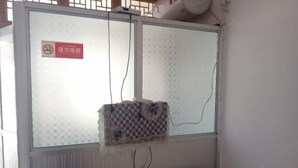 Ein Zimmer mit einem Fenster, das mit einem gemusterten Vorhang verdeckt ist, einem sichtbaren Stromkabel und einem Schild mit einem Rauchverbot-Symbol.